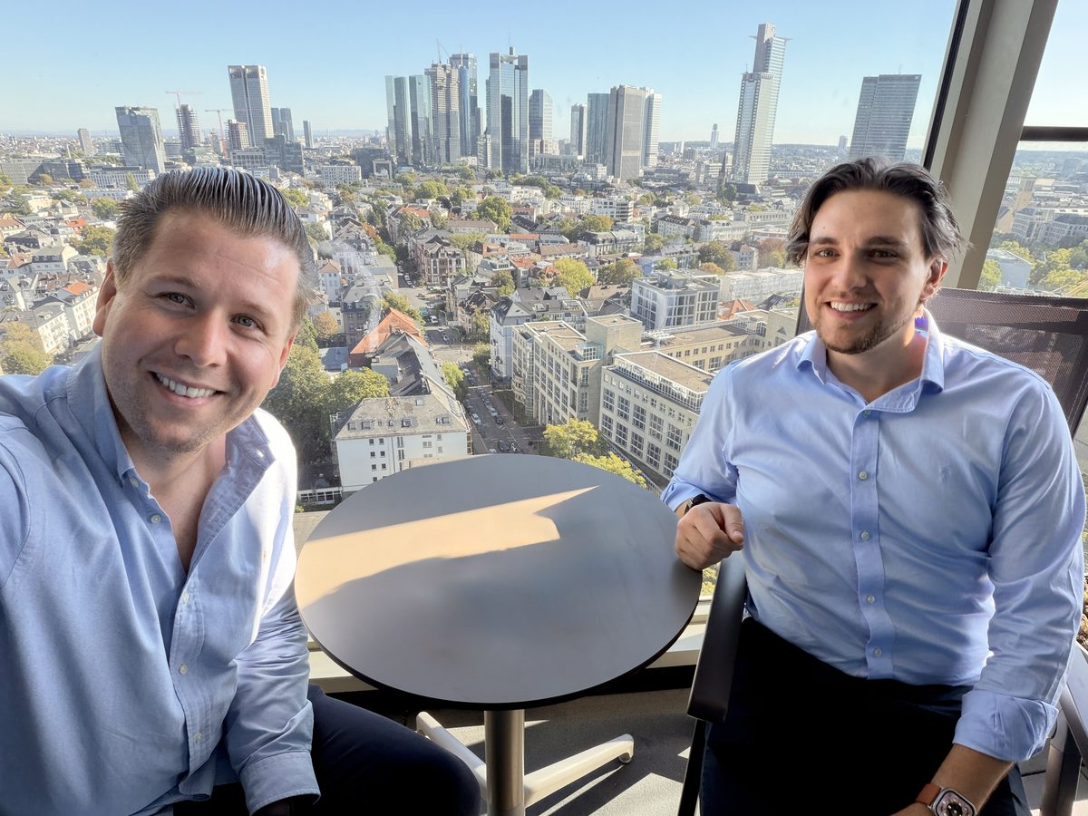 Christian Albert und Christian Nischke an einem Tisch vor der Skyline von Frankfurt